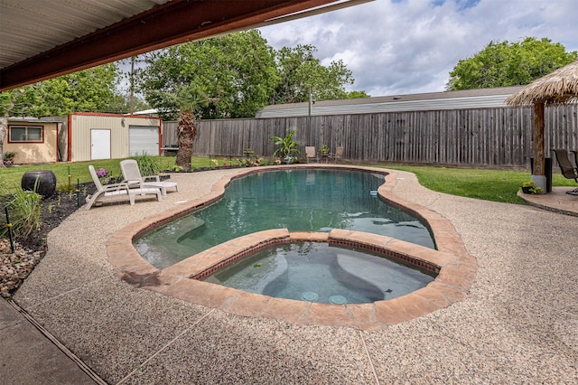 view of swimming pool with a patio, a fenced backyard, a pool with connected hot tub, and an outdoor structure