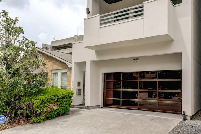 view of exterior entry with concrete driveway, an attached garage, a balcony, and stucco siding