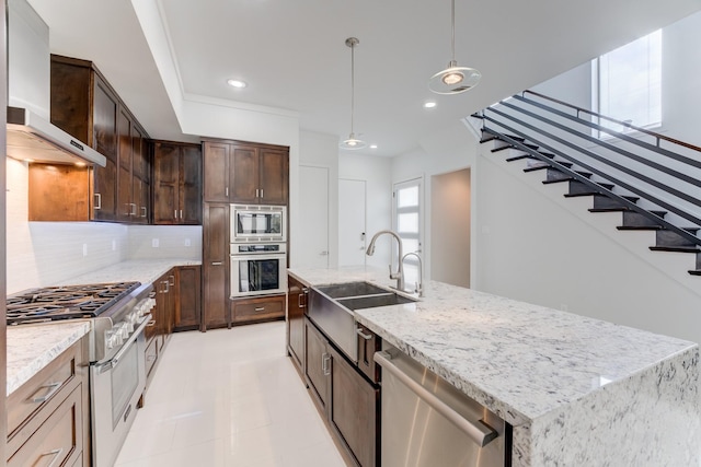 kitchen featuring wall chimney range hood, decorative backsplash, a sink, stainless steel appliances, and an island with sink