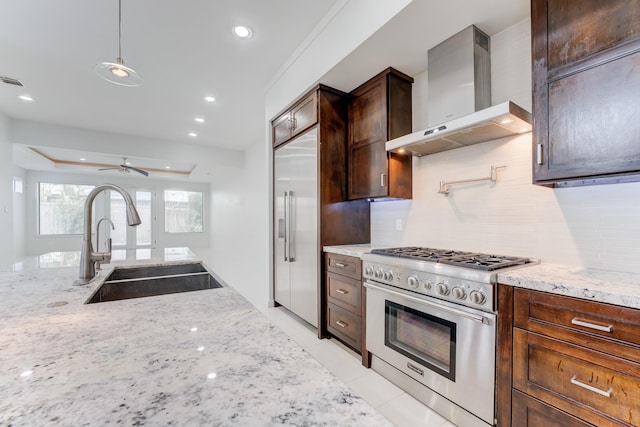 kitchen with decorative backsplash, wall chimney range hood, high quality appliances, light stone counters, and a sink