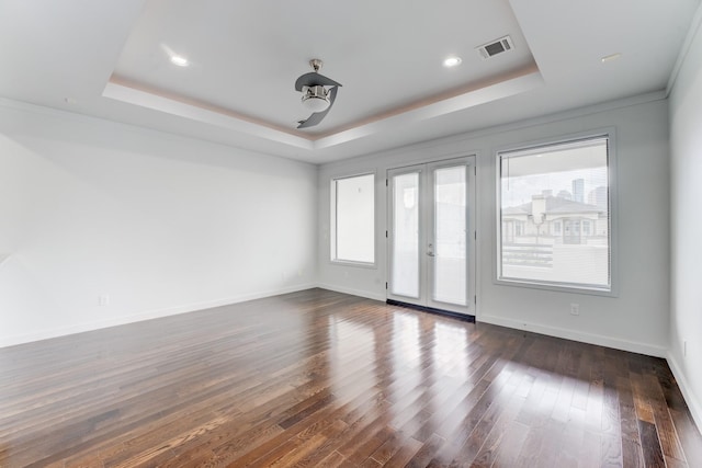 empty room featuring visible vents, dark wood-style flooring, plenty of natural light, and a tray ceiling