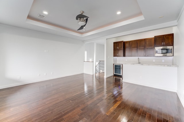 unfurnished living room with a raised ceiling, beverage cooler, dark wood finished floors, visible vents, and bar area