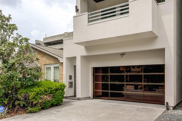 view of exterior entry featuring a garage, stucco siding, a balcony, and concrete driveway