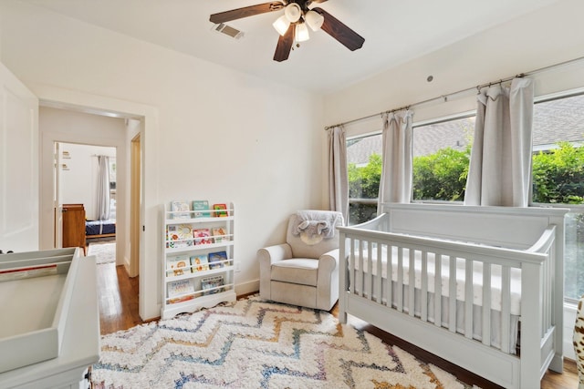 bedroom with wood finished floors, a nursery area, and multiple windows