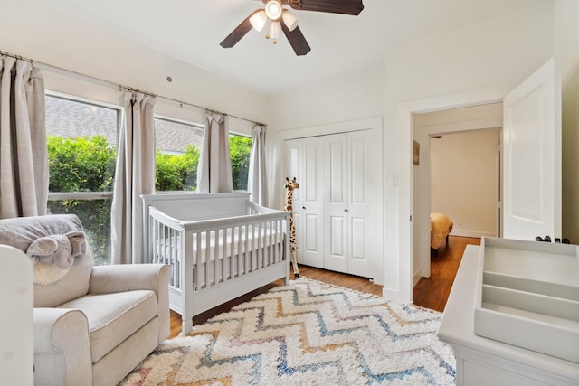 bedroom with a crib, ceiling fan, a closet, and wood finished floors