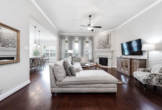 living room with a ceiling fan, crown molding, baseboards, wood-type flooring, and a glass covered fireplace