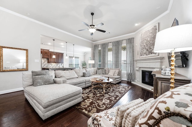 living room featuring ceiling fan, a glass covered fireplace, baseboards, dark wood-type flooring, and ornamental molding