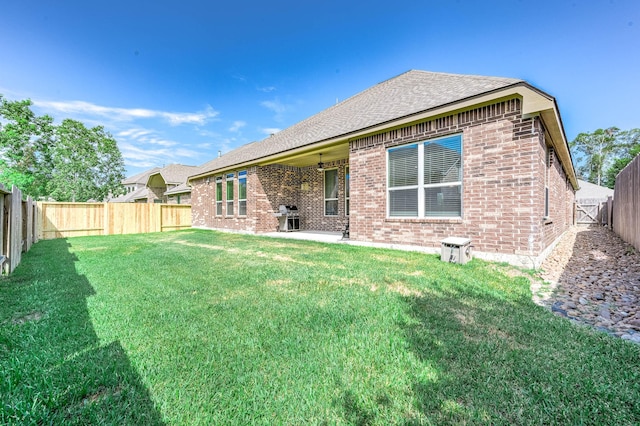 back of house featuring a yard, brick siding, a fenced backyard, and roof with shingles