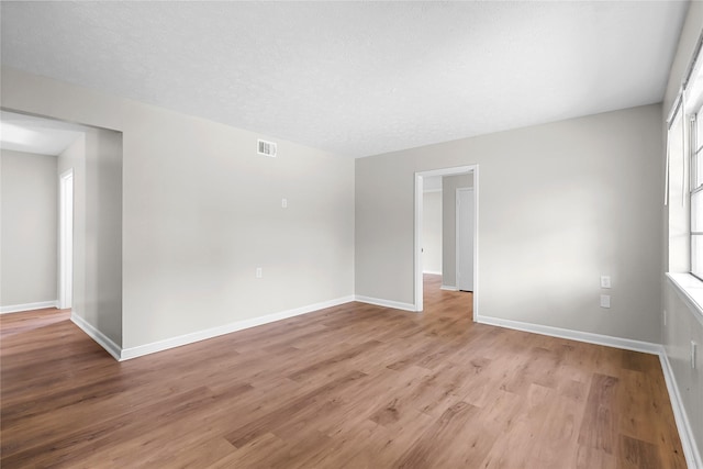 empty room featuring light wood-style floors, baseboards, and visible vents