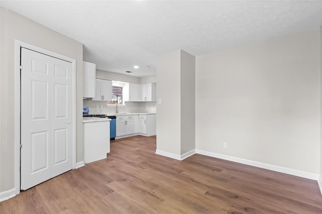 kitchen with baseboards, light countertops, light wood finished floors, and white cabinets