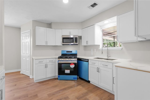 1403 Marilyn St, Conroe, TX 77301 - kitchen with appliances with stainless steel finishes, a sink, white cabinets, light wood-style flooring, and recessed lighting