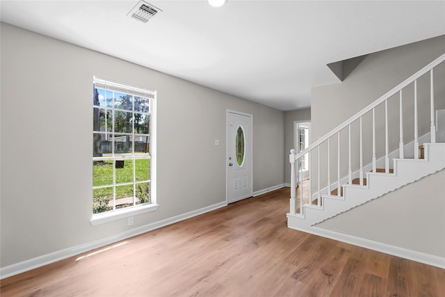 foyer entrance featuring baseboards, visible vents, wood finished floors, and stairway