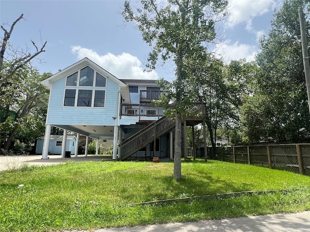 back of house featuring fence, a deck, stairs, a lawn, and a carport