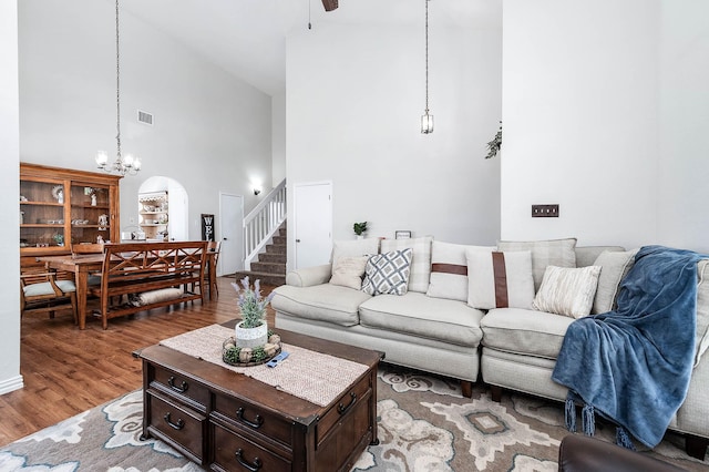 living room with high vaulted ceiling, a chandelier, wood finished floors, visible vents, and stairway