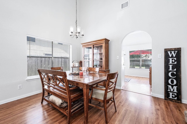 dining space with visible vents, arched walkways, wood finished floors, baseboards, and an inviting chandelier
