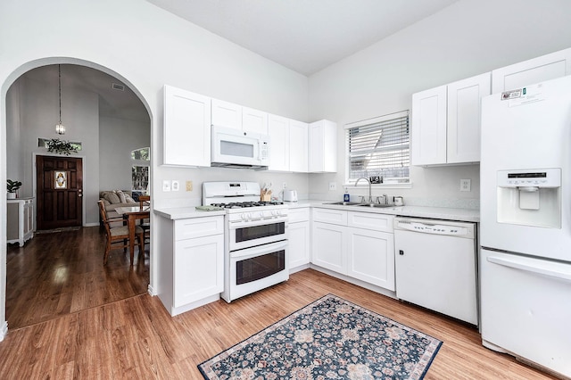 kitchen featuring a sink, light wood finished floors, white appliances, arched walkways, and light countertops