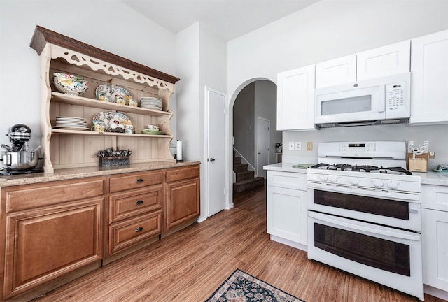 kitchen with white appliances, arched walkways, white cabinets, and light wood-style floors