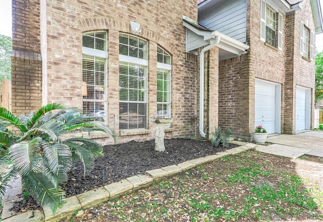 property entrance with a garage, concrete driveway, and brick siding