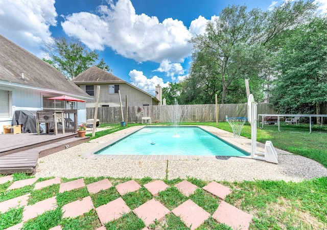 view of pool featuring a trampoline, a lawn, a wooden deck, a fenced in pool, and a fenced backyard