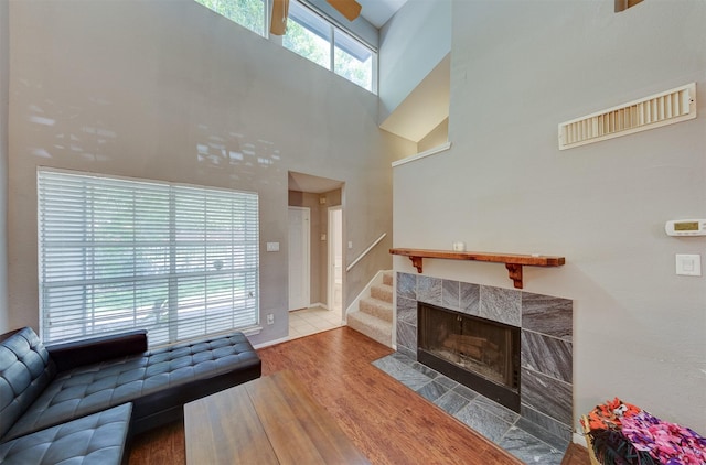 living area with a tiled fireplace, baseboards, wood finished floors, and a towering ceiling