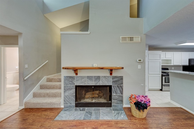 living area featuring visible vents, baseboards, stairway, a tiled fireplace, and light wood-style flooring