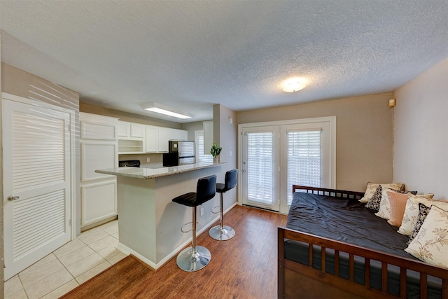 kitchen featuring a kitchen bar, a textured ceiling, white cabinets, a peninsula, and light wood finished floors