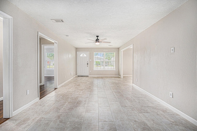 unfurnished living room with a ceiling fan, a textured ceiling, visible vents, baseboards, and a textured wall
