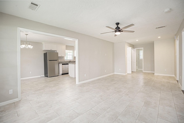 unfurnished living room with a textured ceiling, visible vents, light tile patterned floors, baseboards, and ceiling fan with notable chandelier