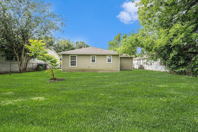 rear view of house featuring fence, a shingled roof, and a yard