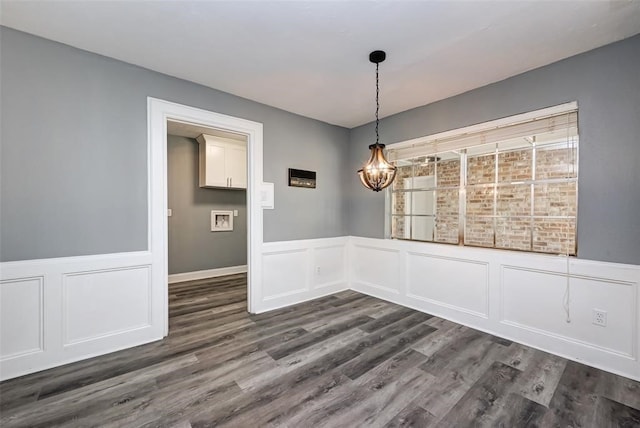 unfurnished dining area with an inviting chandelier, dark wood-style flooring, a decorative wall, and a wainscoted wall