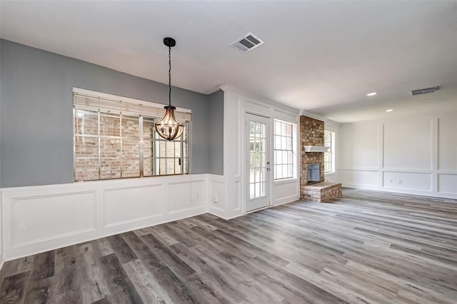 unfurnished dining area featuring an inviting chandelier, a fireplace, a decorative wall, wood finished floors, and visible vents