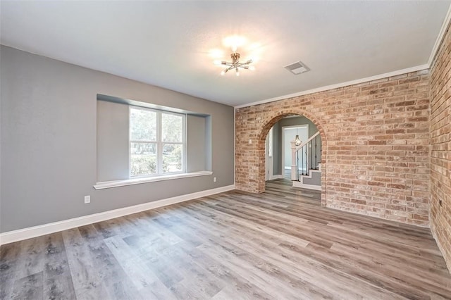 spare room with brick wall, arched walkways, wood finished floors, baseboards, and a notable chandelier