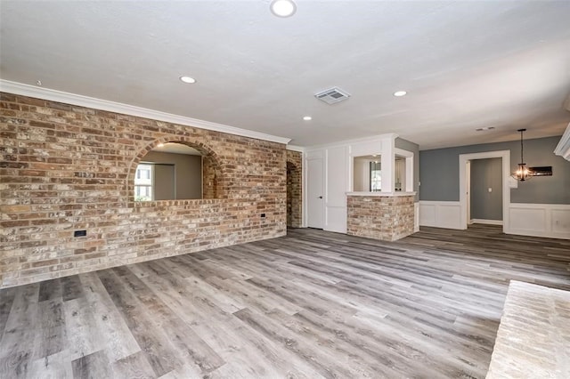 unfurnished living room featuring brick wall, visible vents, wainscoting, wood finished floors, and ornamental molding