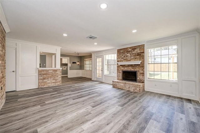 unfurnished living room featuring visible vents, a brick fireplace, a decorative wall, wood finished floors, and recessed lighting