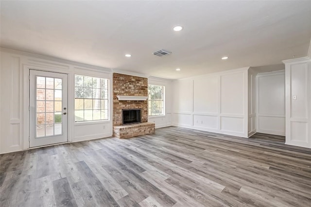 unfurnished living room with visible vents, a brick fireplace, a decorative wall, and wood finished floors