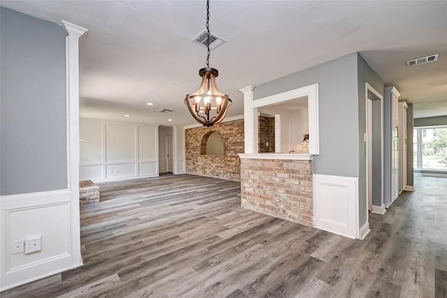 unfurnished dining area featuring a notable chandelier, visible vents, wood finished floors, and a decorative wall