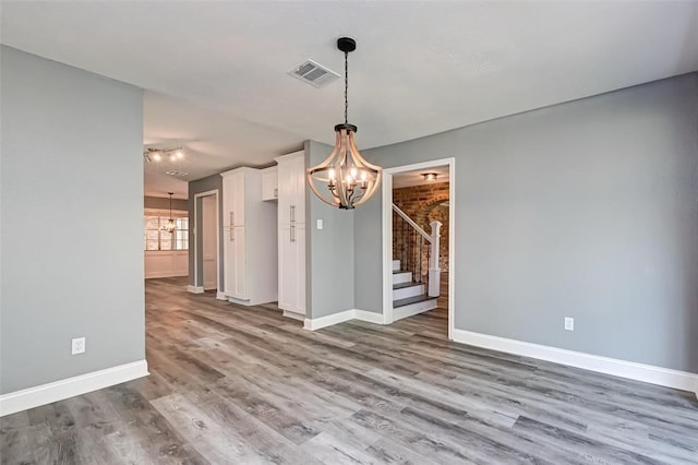 unfurnished dining area with an inviting chandelier, baseboards, stairs, and wood finished floors