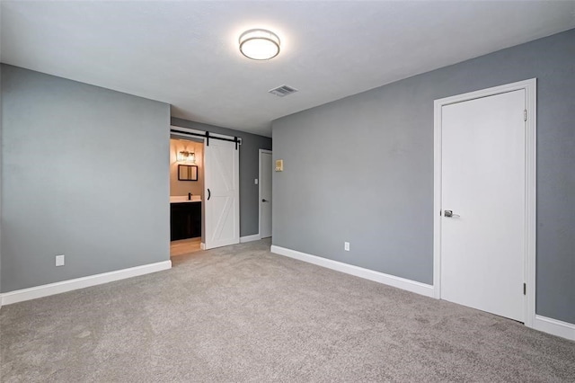 unfurnished bedroom with visible vents, a barn door, baseboards, ensuite bathroom, and carpet flooring
