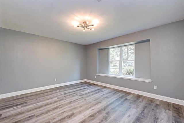 empty room with an inviting chandelier, baseboards, and wood finished floors