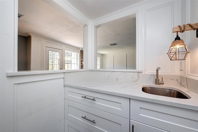 kitchen with a sink, light stone countertops, white cabinetry, and visible vents