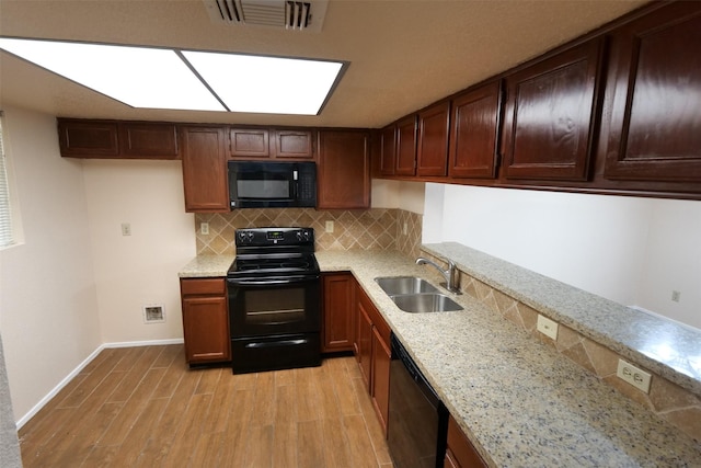 kitchen with light stone countertops, a sink, light wood finished floors, visible vents, and black appliances