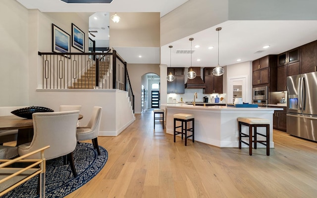 kitchen with dark brown cabinets, light wood-style floors, a breakfast bar area, arched walkways, and stainless steel appliances