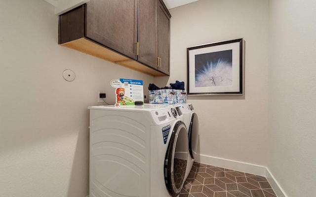 clothes washing area featuring baseboards, cabinet space, dark tile patterned floors, and washing machine and clothes dryer