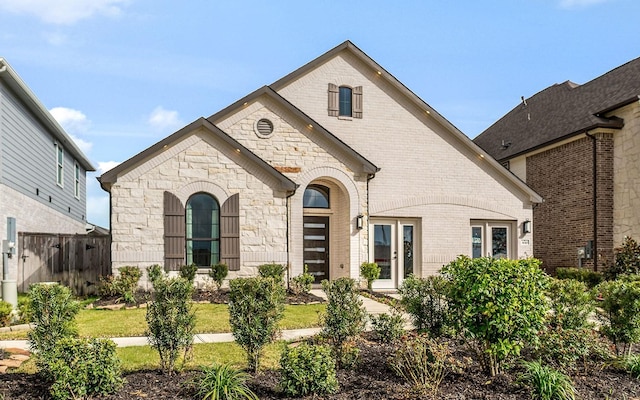 french country style house featuring fence, brick siding, and stone siding