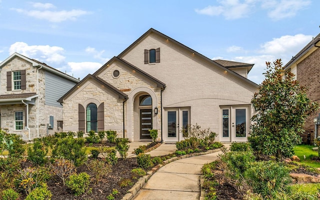 french country inspired facade with brick siding, french doors, and stone siding