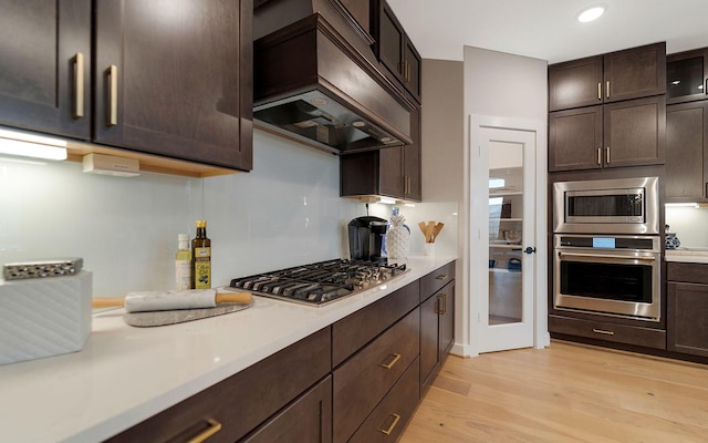 kitchen with light countertops, stainless steel appliances, custom range hood, and light wood-style floors