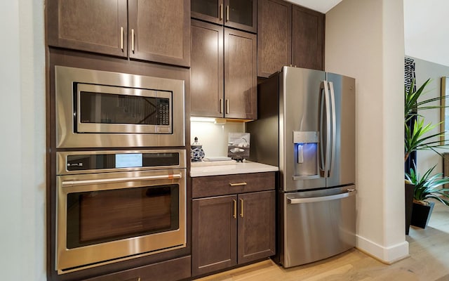 kitchen featuring dark brown cabinetry, appliances with stainless steel finishes, light wood finished floors, light countertops, and baseboards