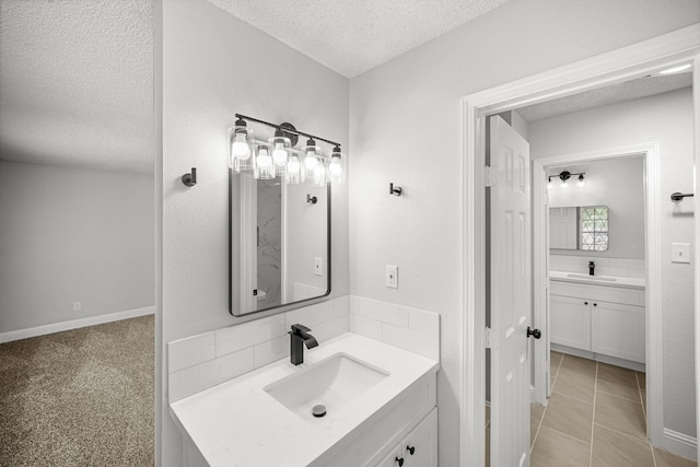 full bath with a sink, tile patterned flooring, a textured ceiling, and two vanities