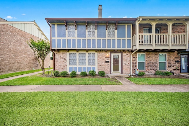 multi unit property featuring brick siding, a front lawn, a balcony, and a chimney