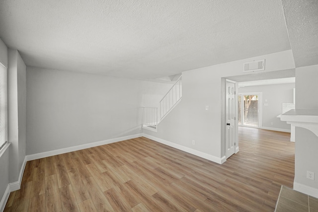 spare room with a textured ceiling, light wood-style flooring, baseboards, visible vents, and stairway